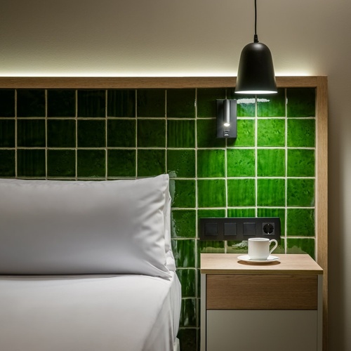 a bedroom with green tiles and a nightstand with a cup of coffee on it