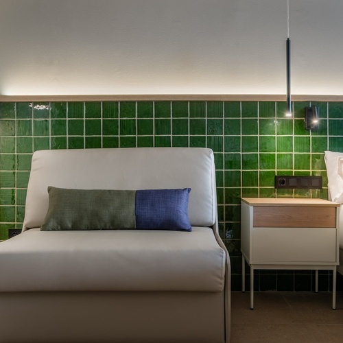 a chair with a blue and green pillow sits next to a bed