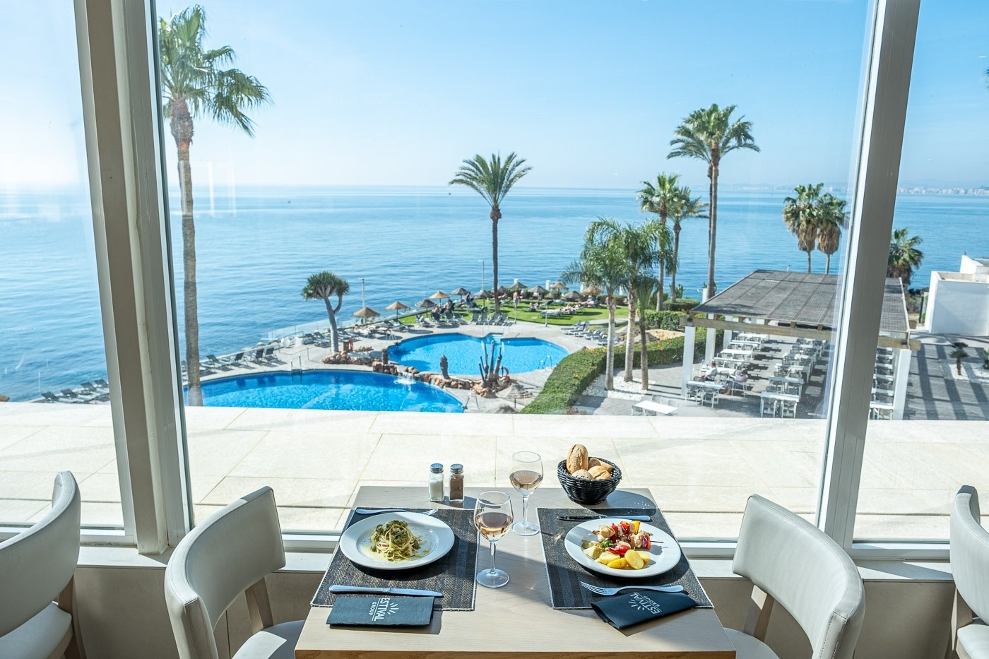 una mesa con platos y copas de vino frente a una ventana con vista al océano