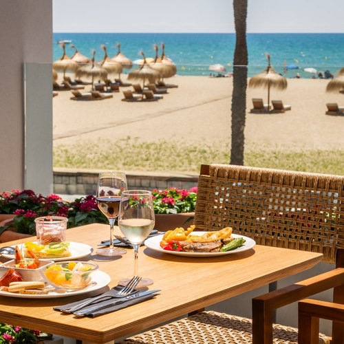 a table with plates of food and glasses of wine with a view of the beach