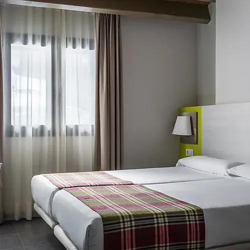 Cozy hotel room with twin beds, plaid runners, and a bright green headboard Hotel Cristina | Andorra | Estival Group | Official Web.