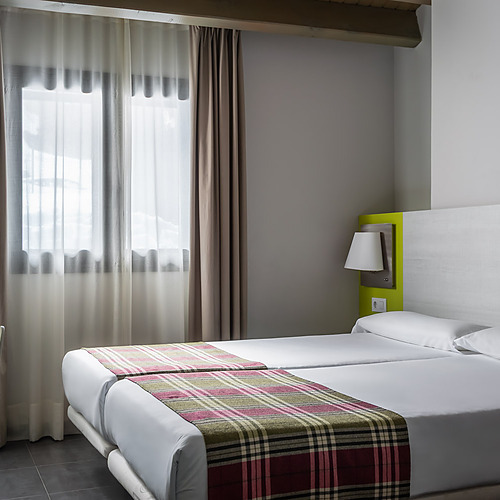 Cozy hotel room with twin beds, plaid runners, and a bright green headboard Hotel Cristina | Andorra | Estival Group | Official Web.