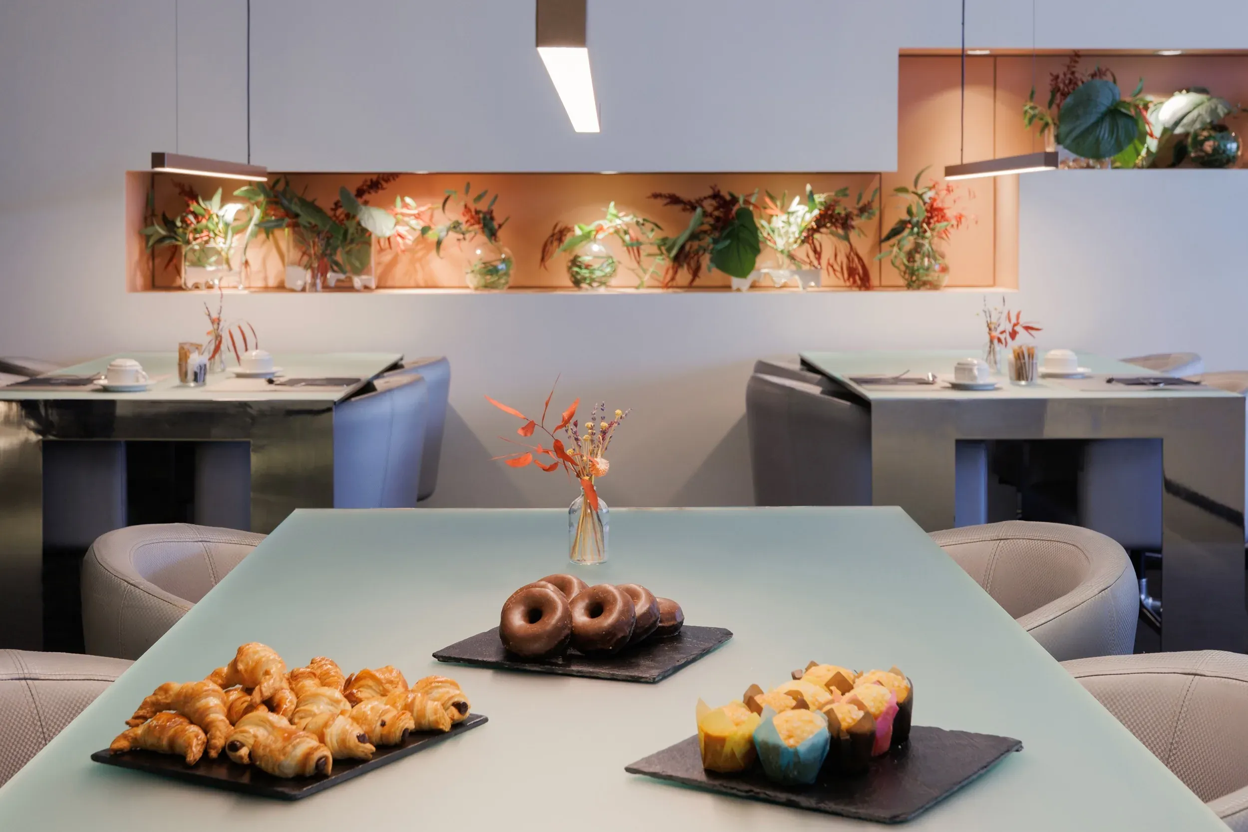 Buffet corporatiu ESTIVAL: Croissants, donuts i muffins sobre taula de vidre.