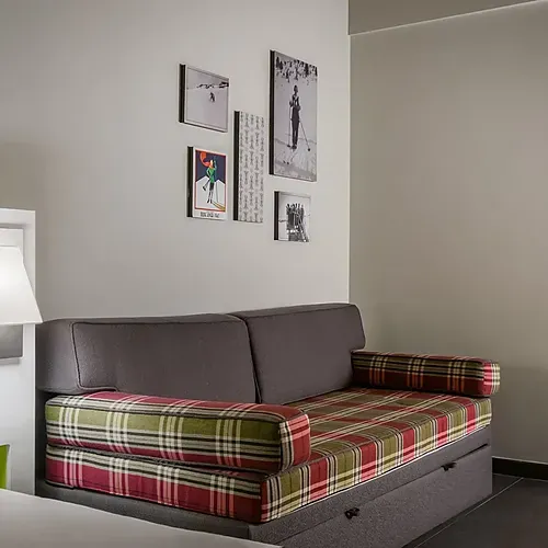 Cozy hotel room with a plaid sofa bed, wall art, and lamp. Hotel Cristina | Andorra | Estival Group | Official Web