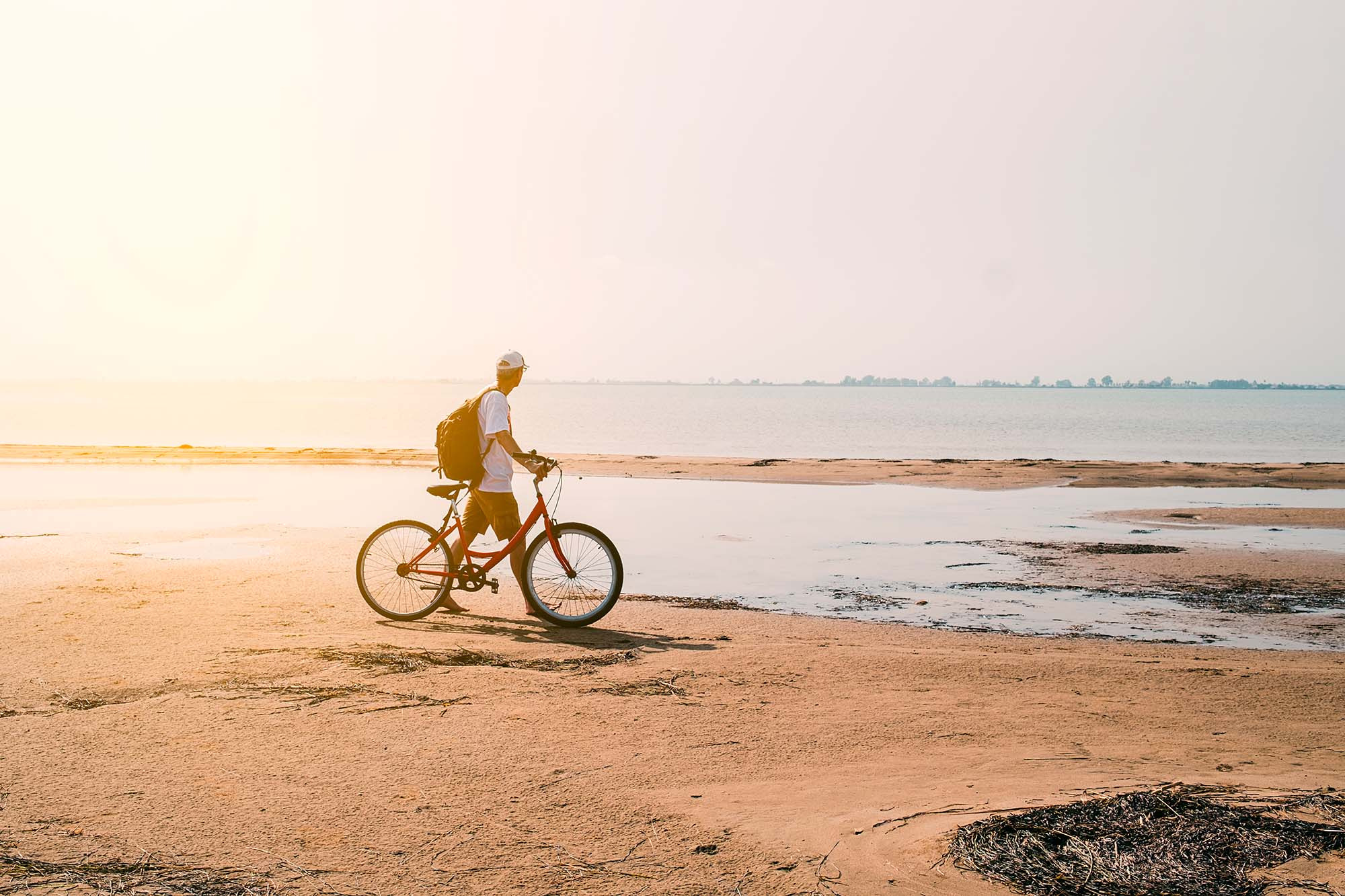 Man with backpack on bike on sandy beach at sunset ESTIVAL: Corporativa
