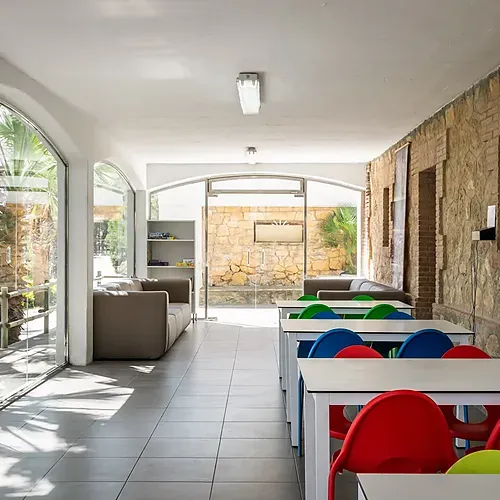 Séjournez à Estival Torre de la Mora : salon lumineux, tables colorées et patio ombragé.