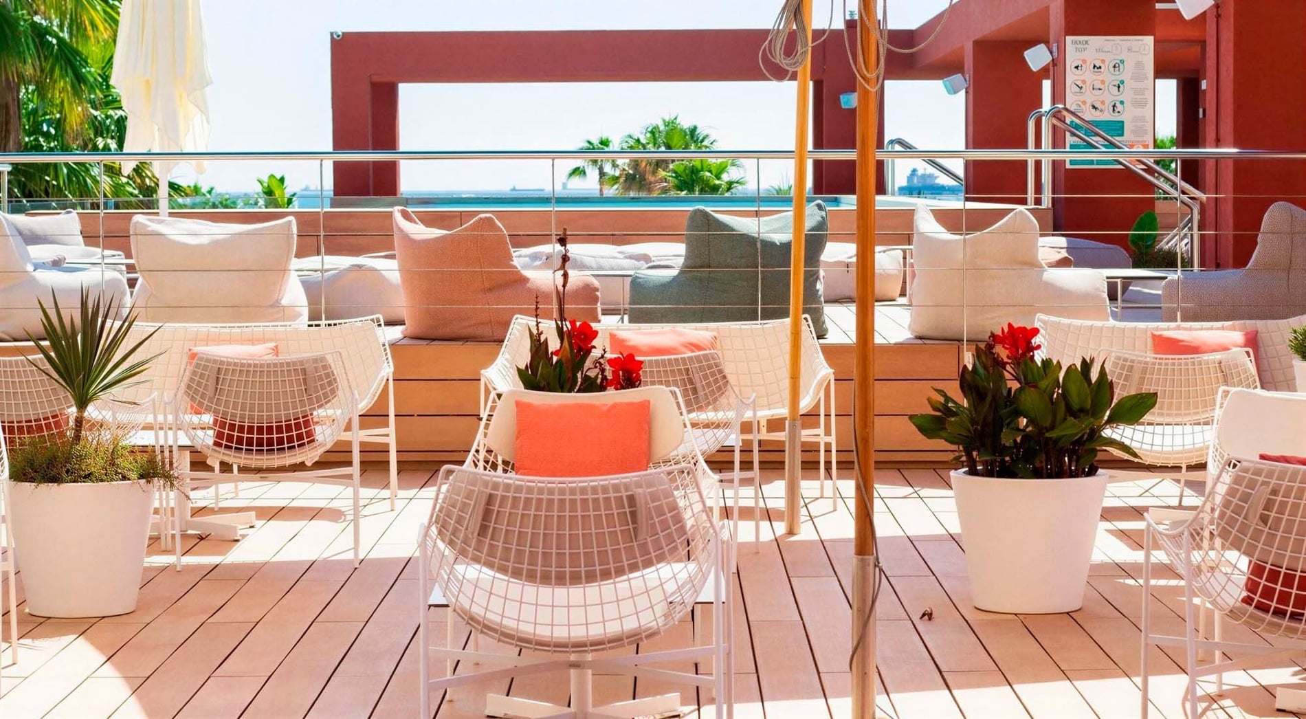 Una terrassa assolellada al terrat amb seients còmodes, plantes en test i vistes al mar i a una piscina.