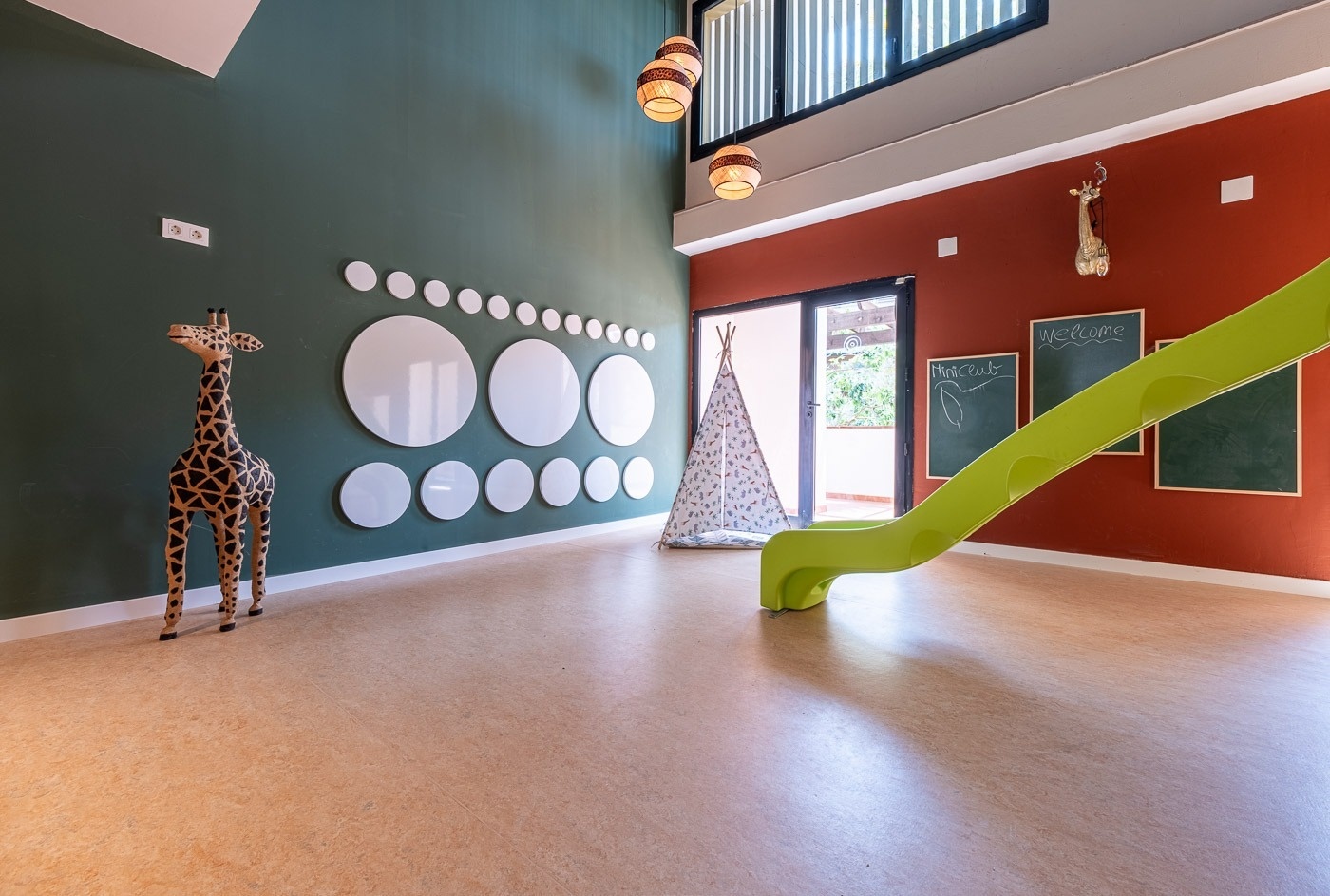 a green slide is in a room with a teepee and circles on the wall