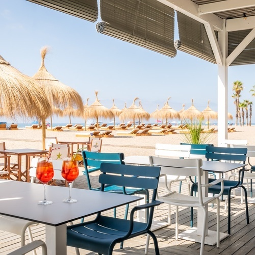 tables and chairs on a beach with straw umbrellas