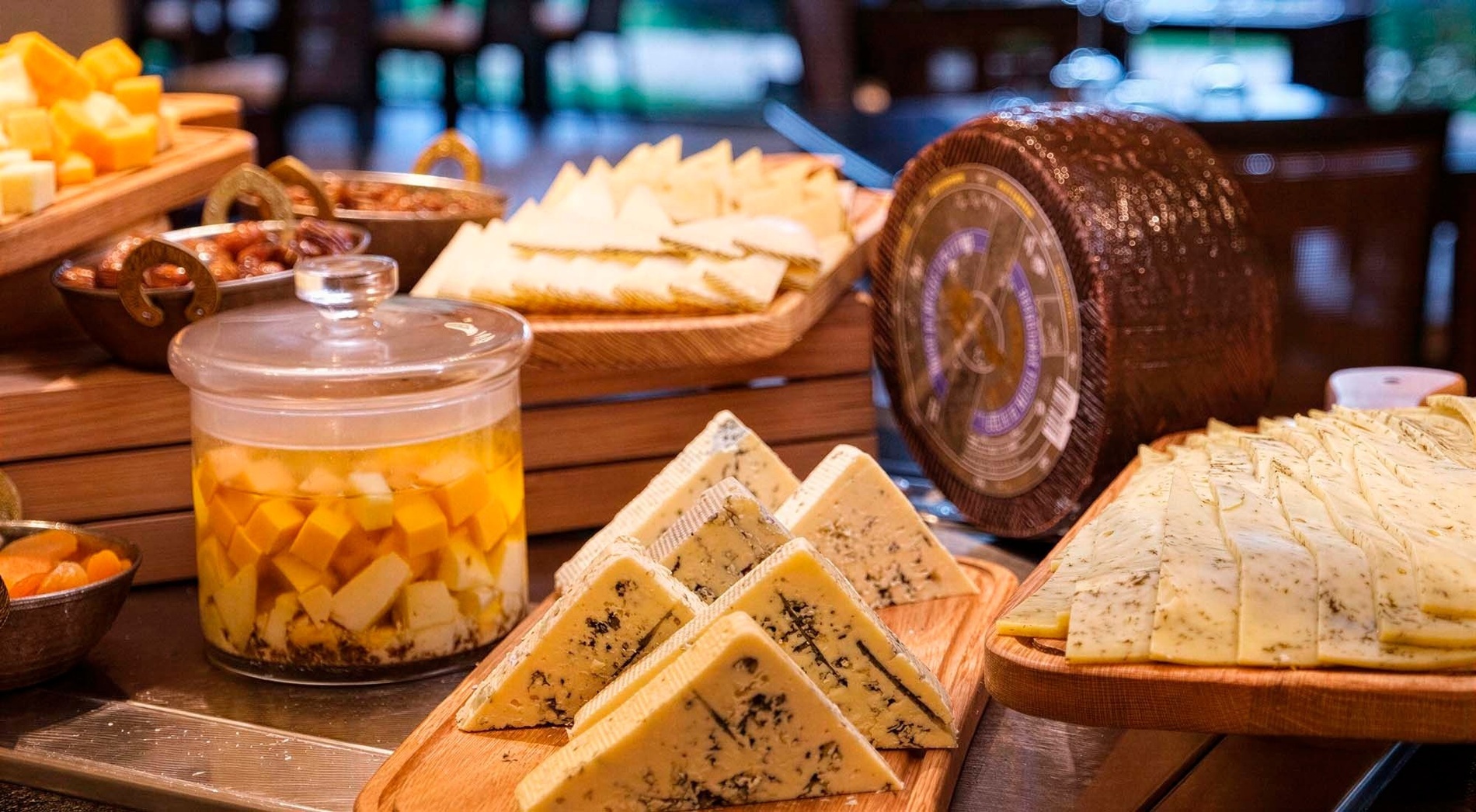 A diverse cheese buffet is displayed, featuring various sliced cheeses, blue cheese wedges, and cubed cheese in oil, alongside other appetizers.