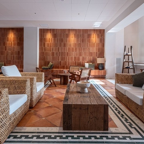 This inviting interior features a lounge area with woven rattan furniture, a rustic tiled floor, and an illuminated terracotta brick accent wall.