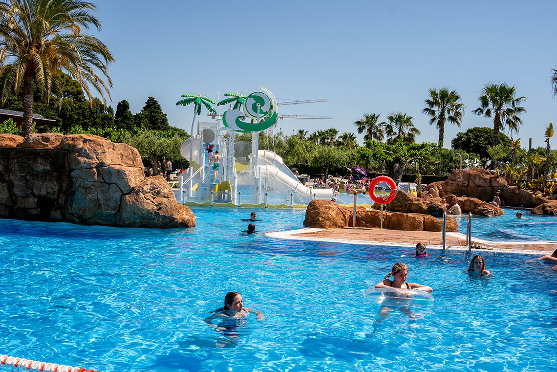 Piscine d'un hôtel avec toboggans et palmiers, endroit idéal pour se détendre ESTIVAL: Corporativa.