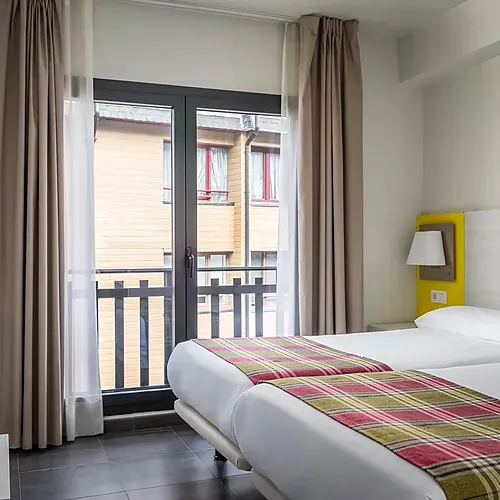 Modern hotel room with two beds, plaid runner & wardrobe at Hotel Cristina | Andorra | Estival Group