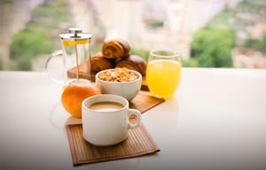 a cup of coffee a bowl of cereal an orange and a glass of orange juice on a table