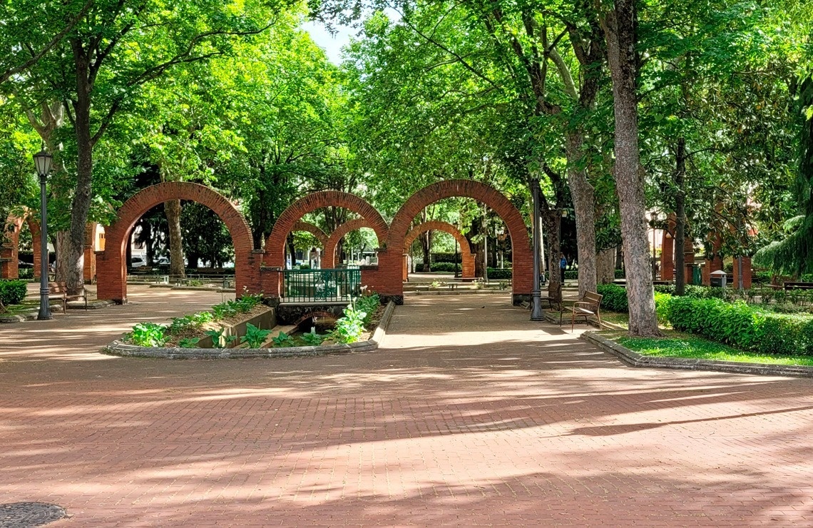 a brick walkway in a park with arches and trees