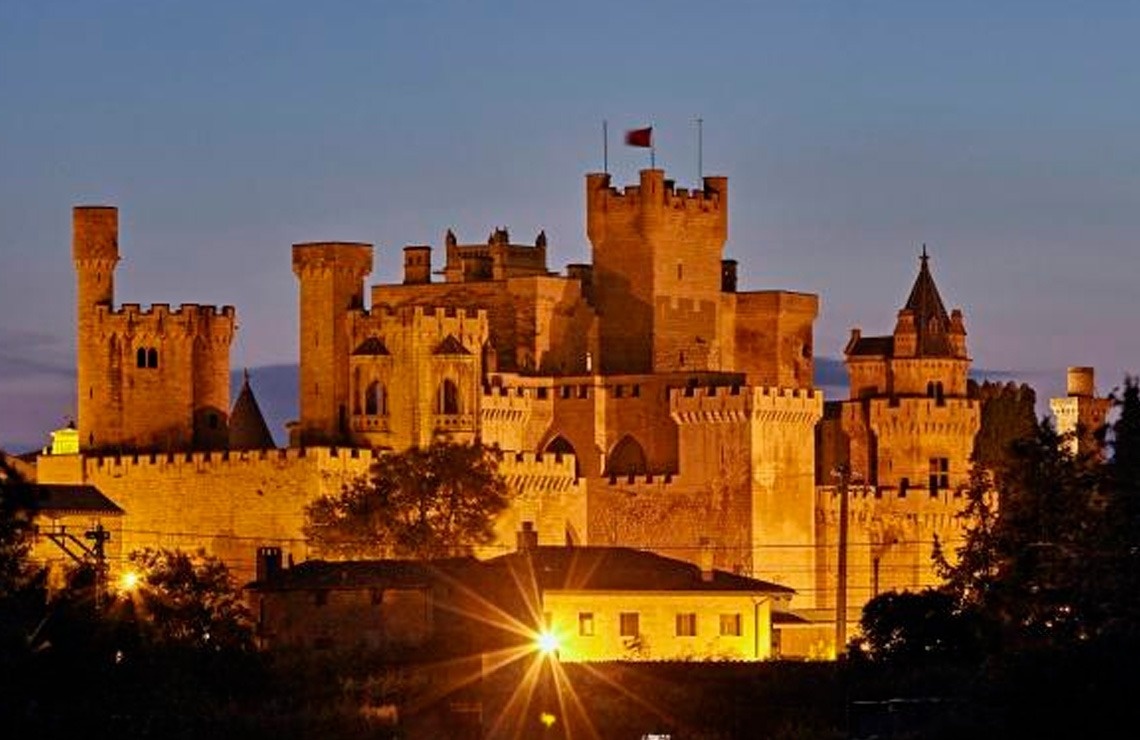 a large building in the middle of a forest with mountains in the background