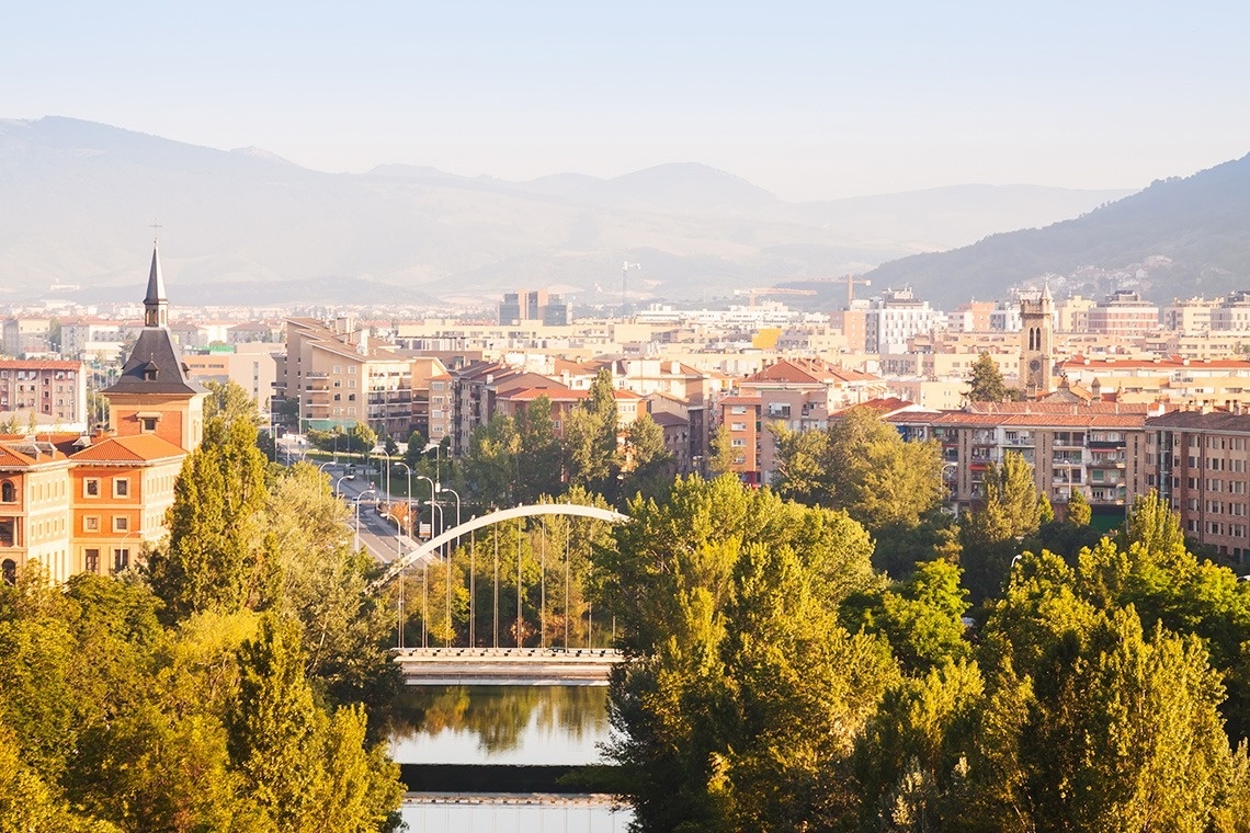 a bridge over a river in a city with mountains in the background