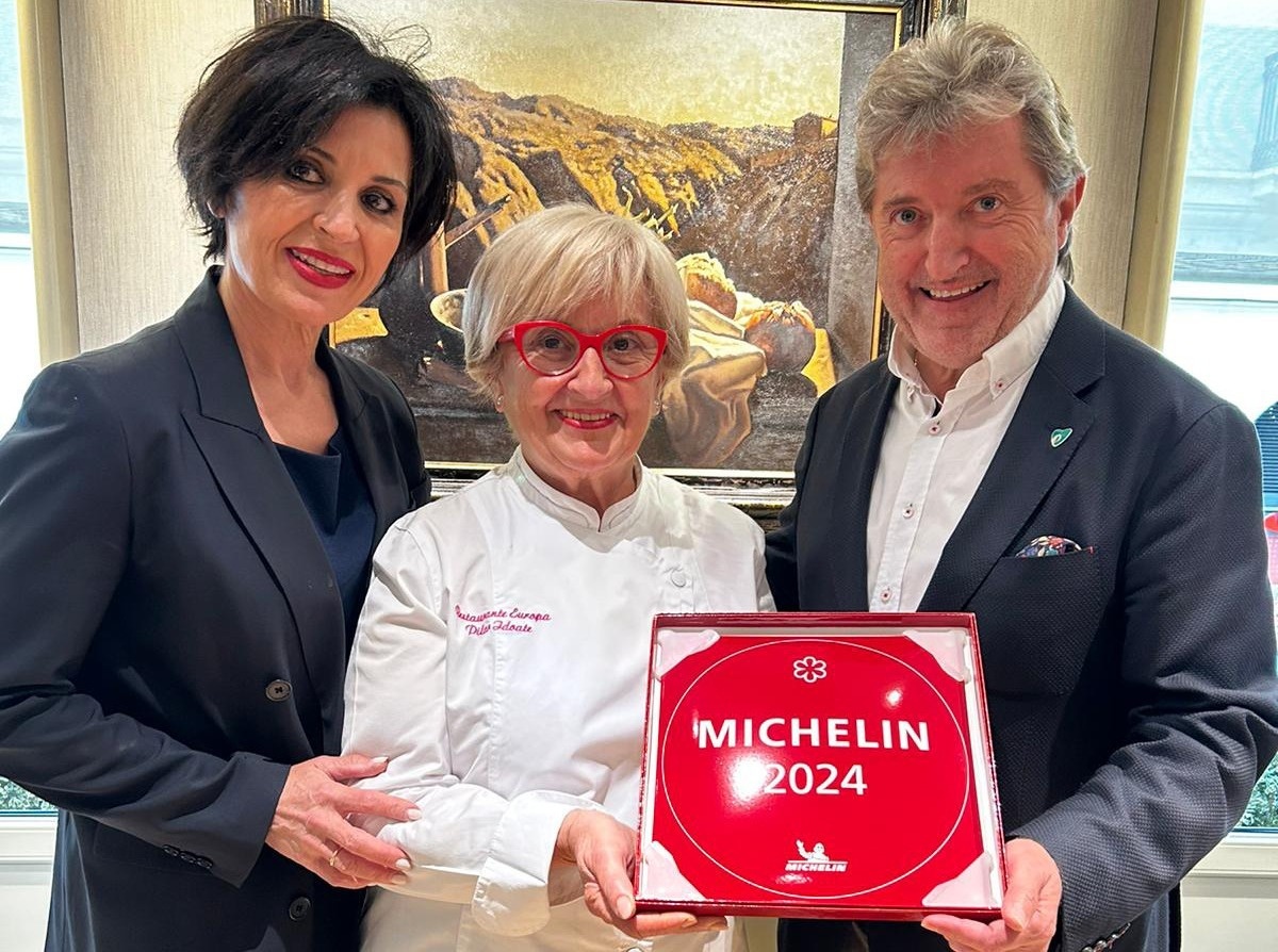 dos mujeres y un hombre sostienen un cartel rojo que dice michelin 2024