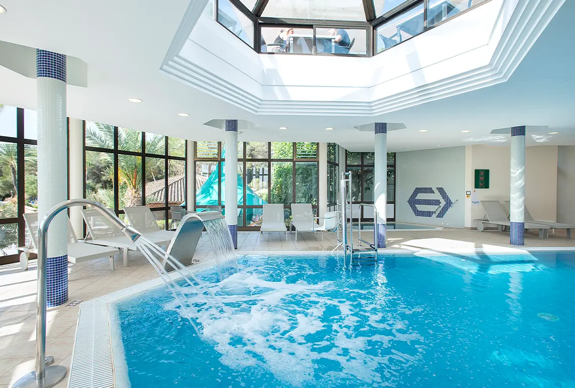 Hotel Exagon Park: piscina interior d'hotel amb zona de solàrium i cascada.