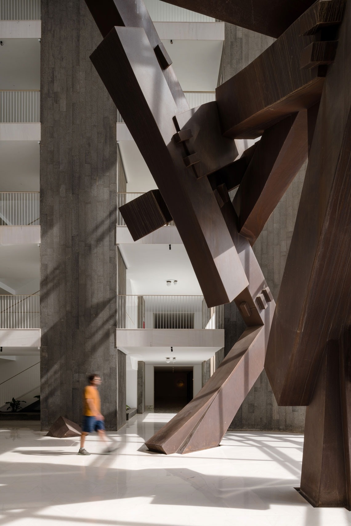 a man in an orange shirt walks past a large sculpture