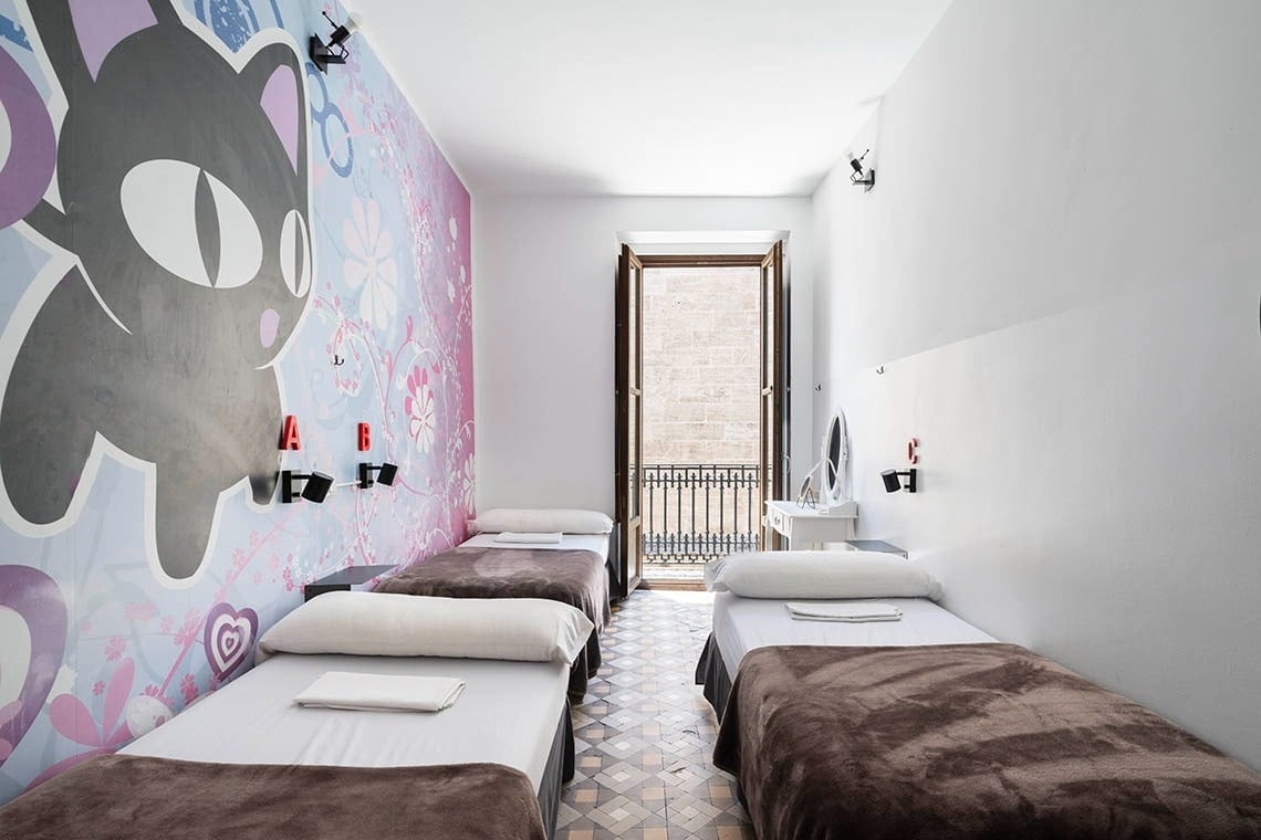 Cozy dorm room at Hôme Youth Hostel Valencia with fun cat mural, twin beds, and balcony.