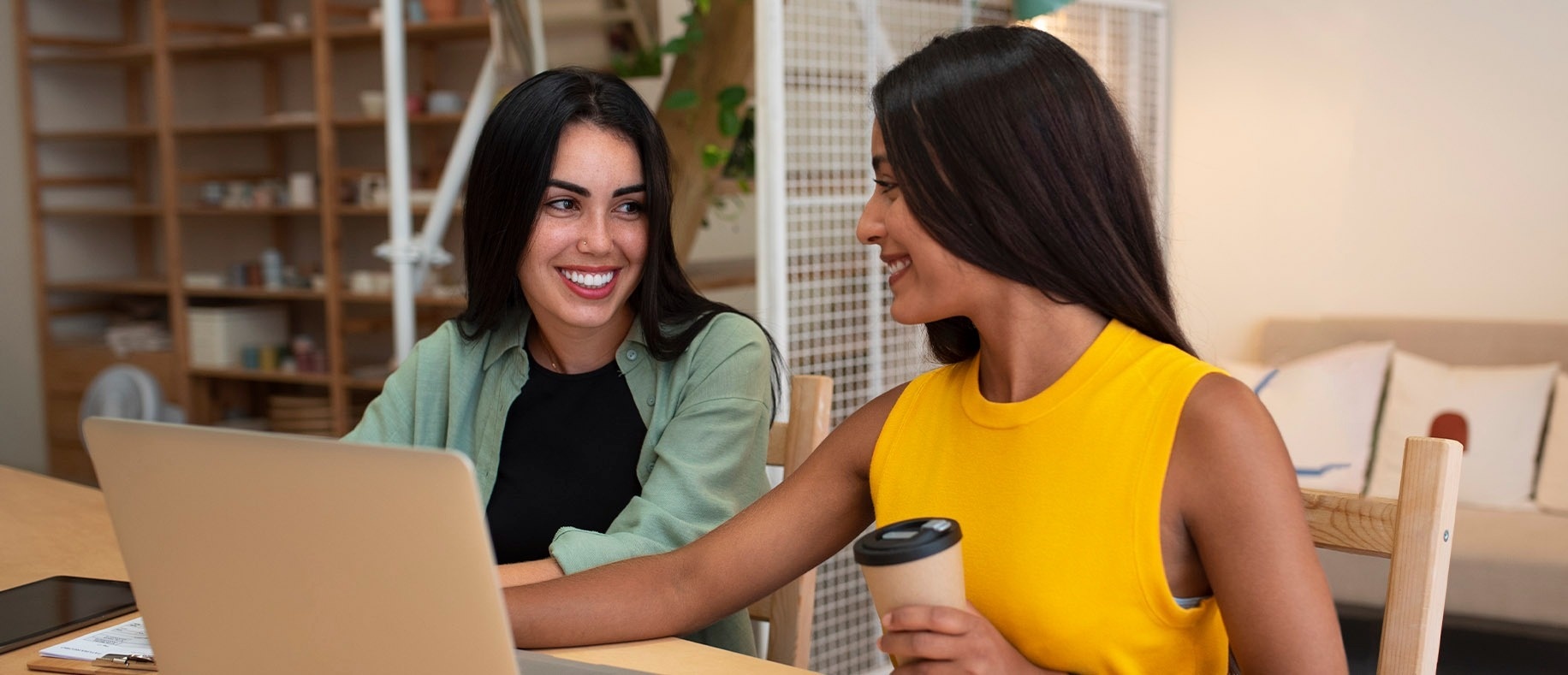 Two women smiling at a laptop, perfect for work or relaxation. Feet up: Corporativa!