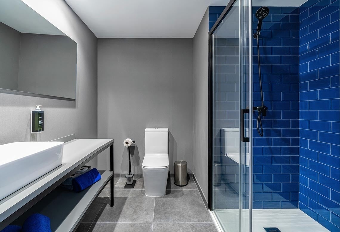 Baño moderno con ducha de vidrio y azulejos azules en el Nest Style Valencia Hotel.