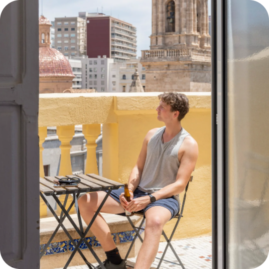 Young man relaxing with beer on balcony, feet up, perfect for your corporate stay.
