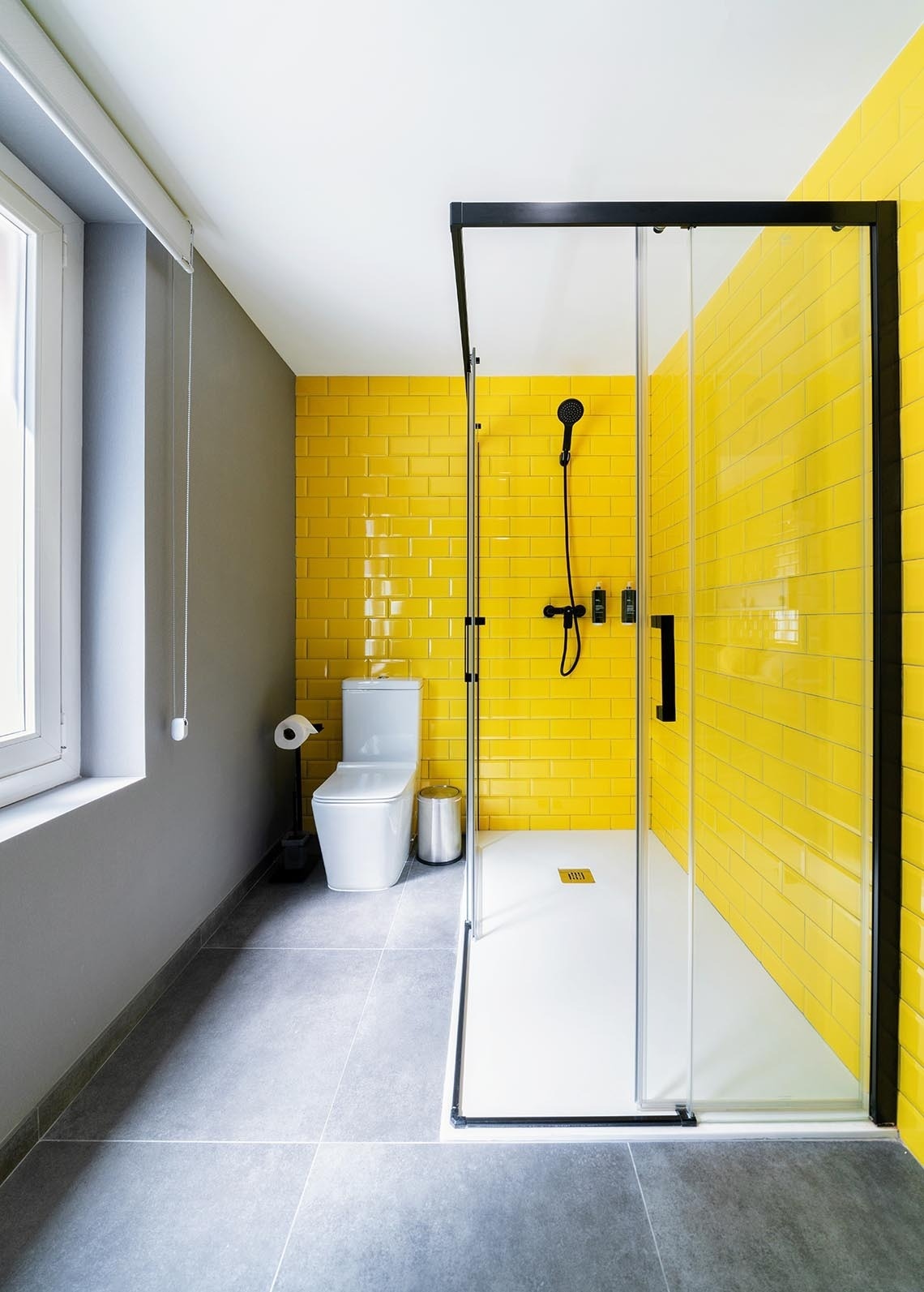 Baño moderno con ducha amarilla y paredes de baldosas en Nest Style Valencia Hotel.