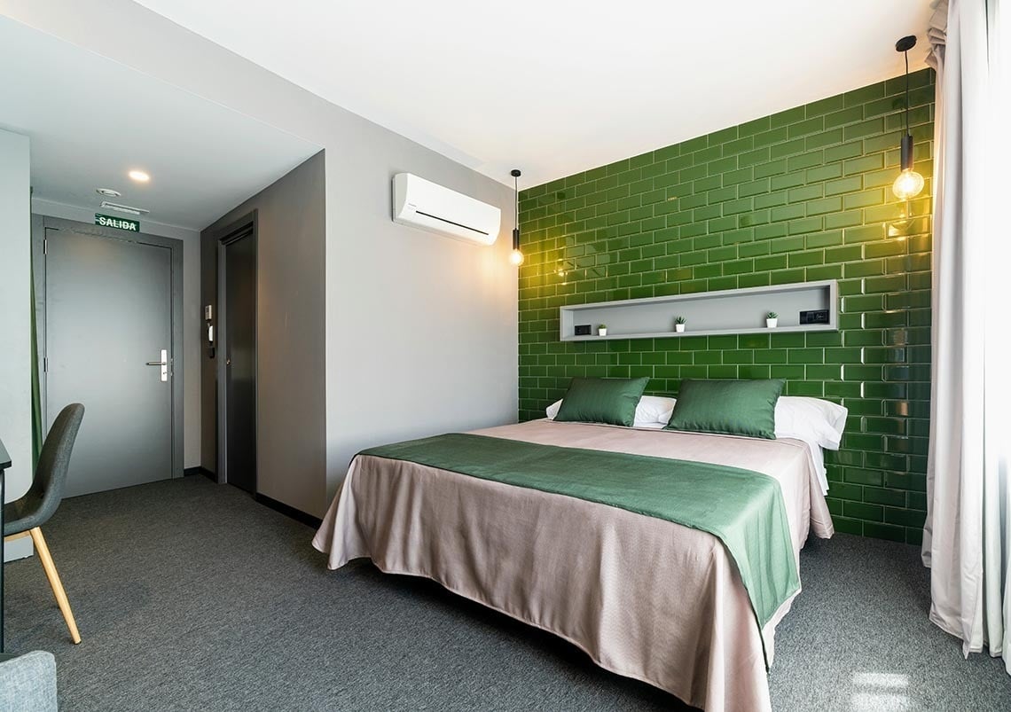 Habitación moderna en Nest Style Valencia Hotel con cama doble y pared de azulejos verdes.