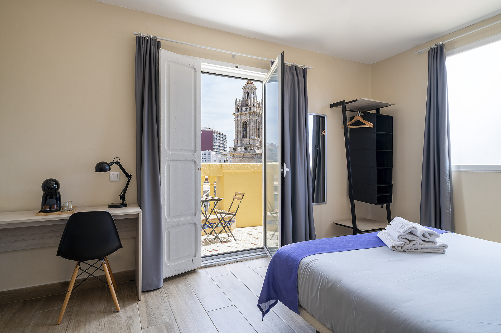 Modern hotel room with a balcony view of a historic tower, queen bed, desk, and coffee maker. Purple Nest Hostel Valencia | Feet Up | Valencia | Official website