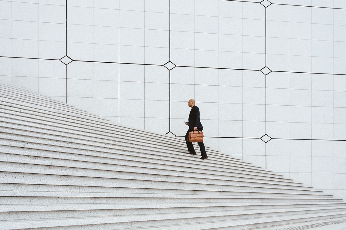 Businessman climbing stairs with briefcase and phone. Feet up: corporate!