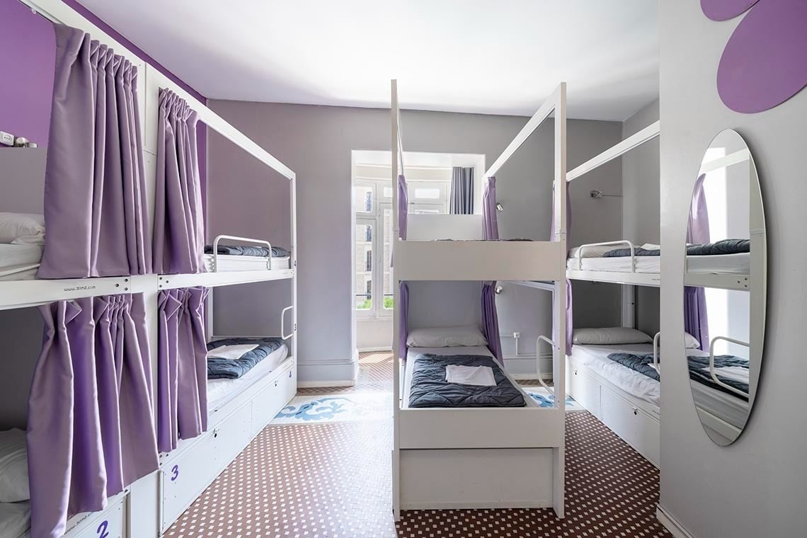 Literas con cortinas púrpuras en Purple Nest Hostel Valencia, ideal para viajeros.