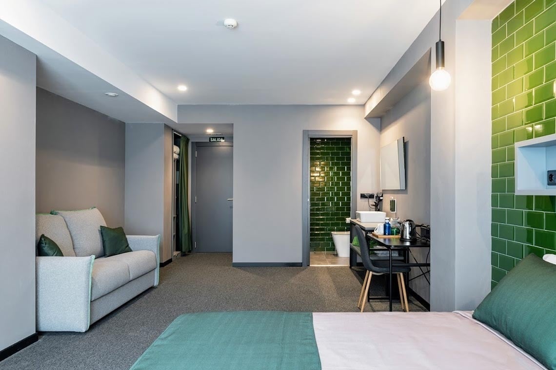 Habitación moderna Nest Style Valencia Hotel con sofá y baño verde esmeralda.