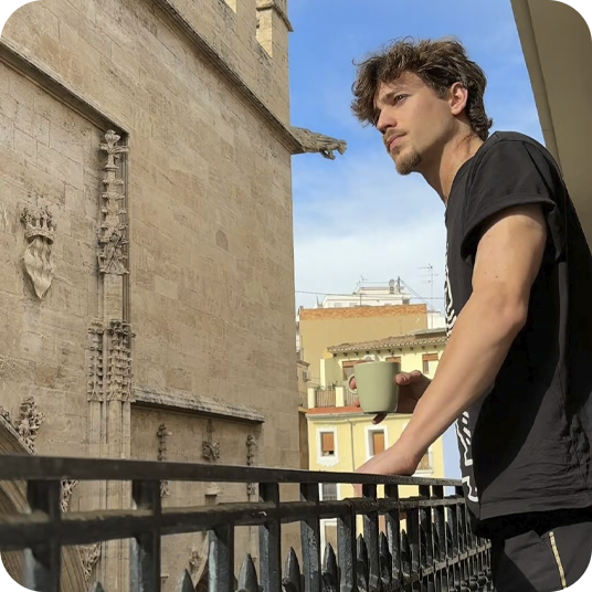 Young man with coffee on balcony, architectural views, feet up: corporate relaxation.