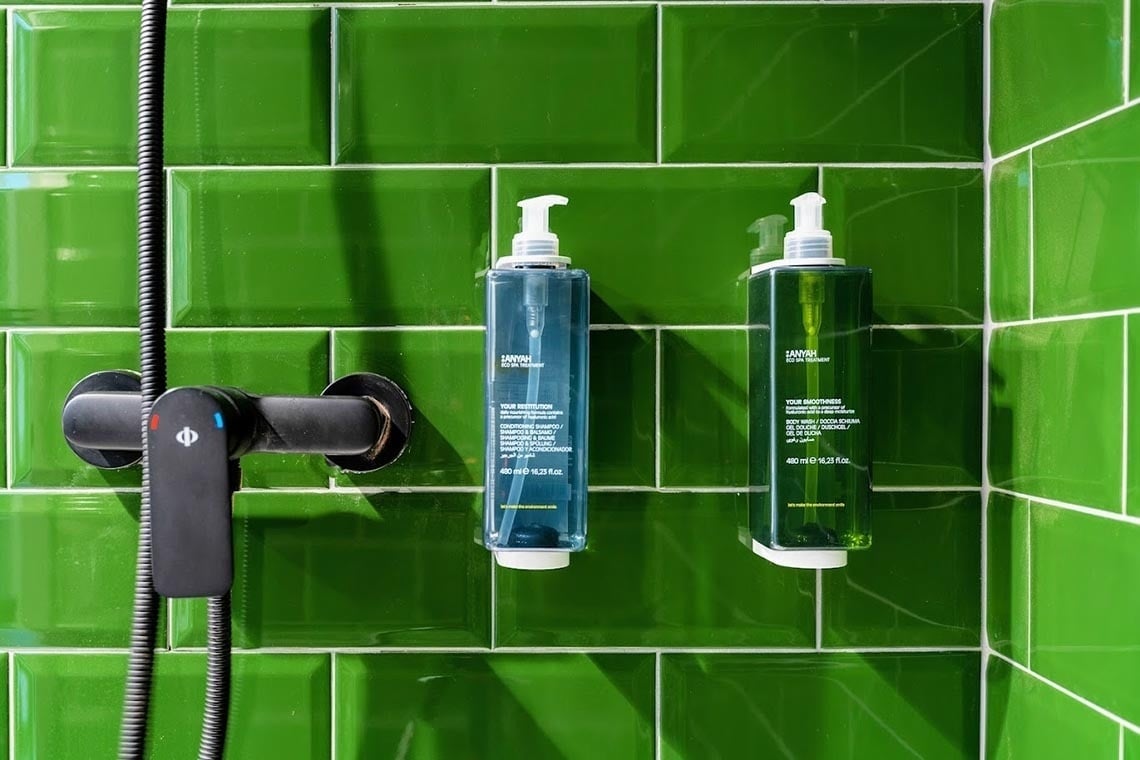 Ducha con jabón y champú ANYAH en azulejos verdes. Nest Style Valencia Hotel | Web oficial.
