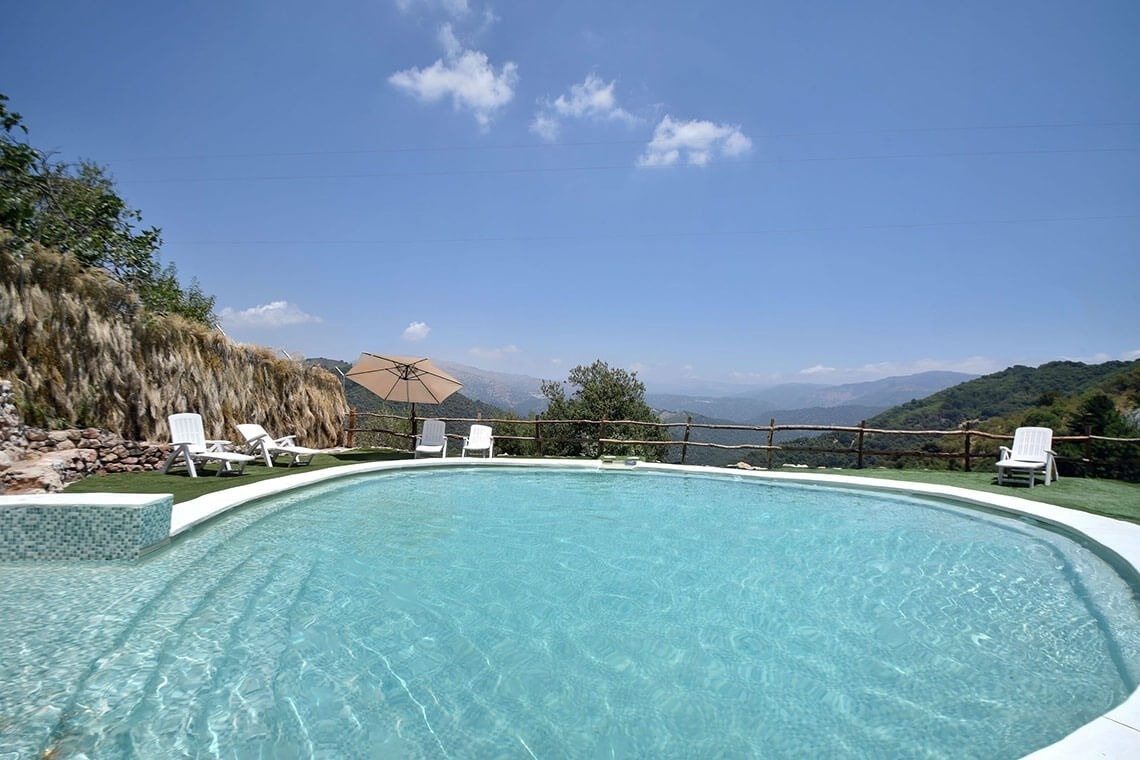 a swimming pool with chairs and an umbrella in the background