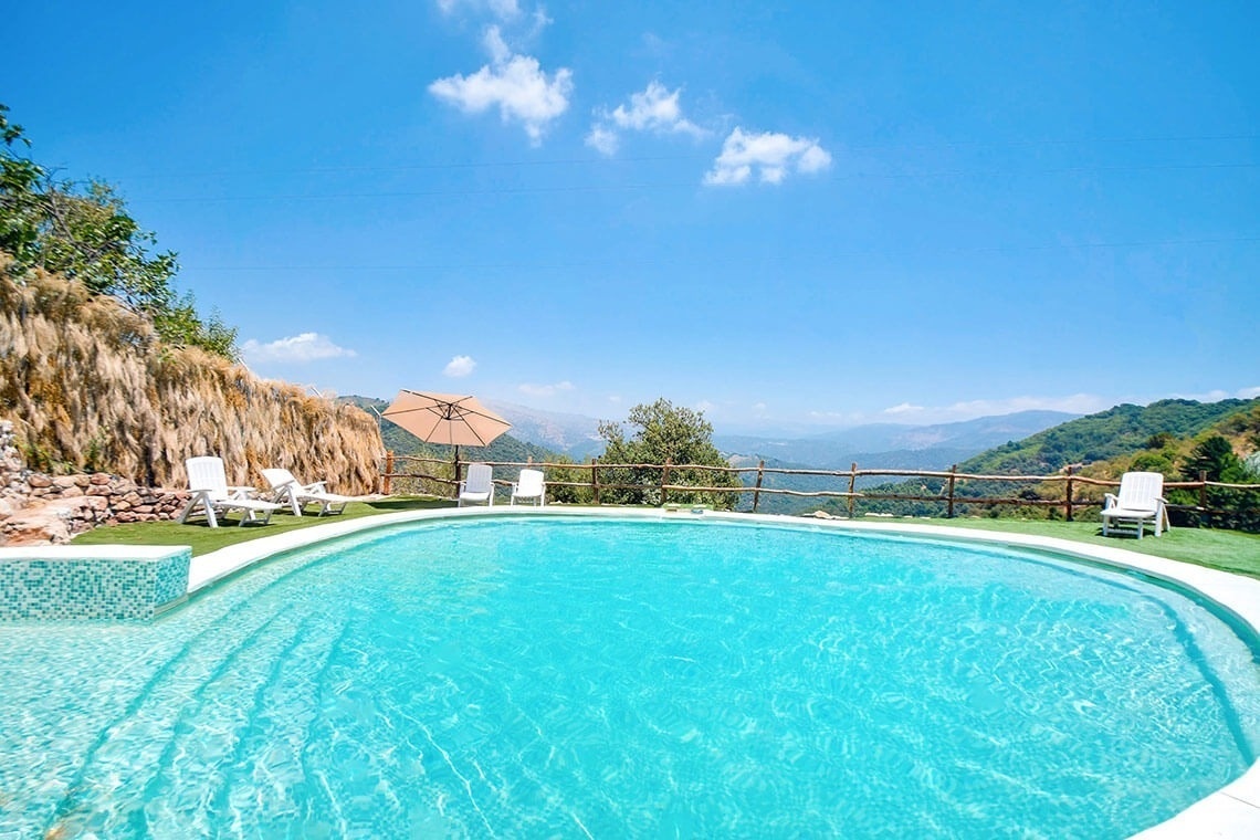 una piscina rodeada de sillas y un paraguas con vistas a las montañas