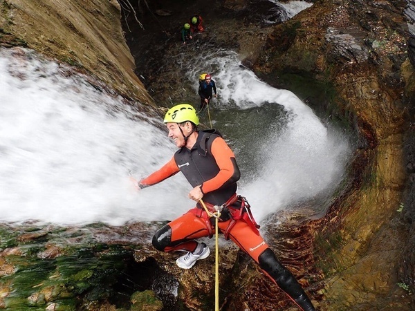 un hombre con un traje de neopreno y un casco amarillo camina por una cascada