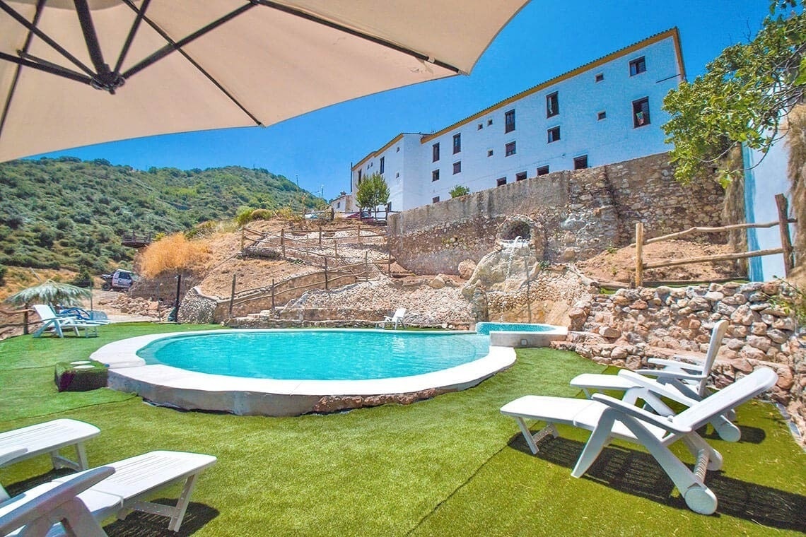 una piscina rodeada de sillas y un paraguas con un edificio blanco en el fondo