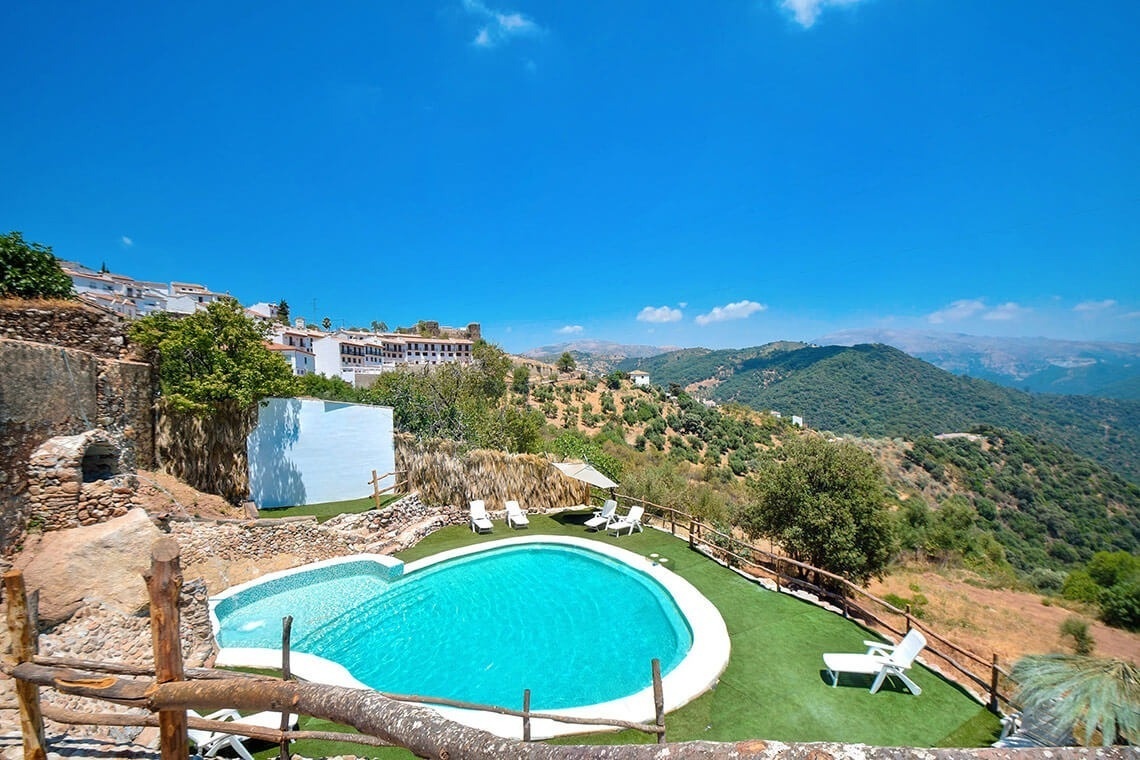 una piscina rodeada de sillas y un edificio blanco en la cima de una colina