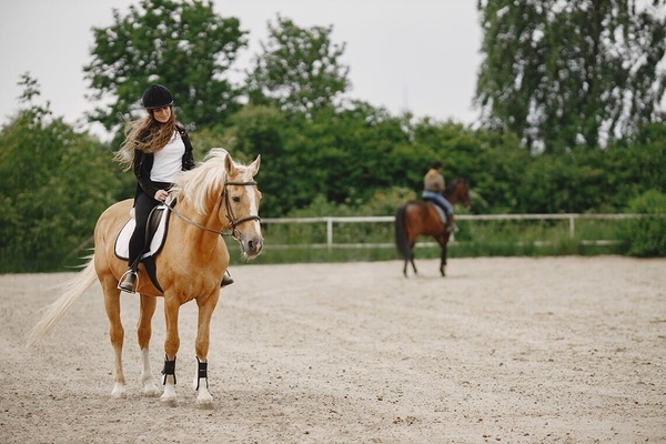 una mujer monta un caballo en un campo de arena