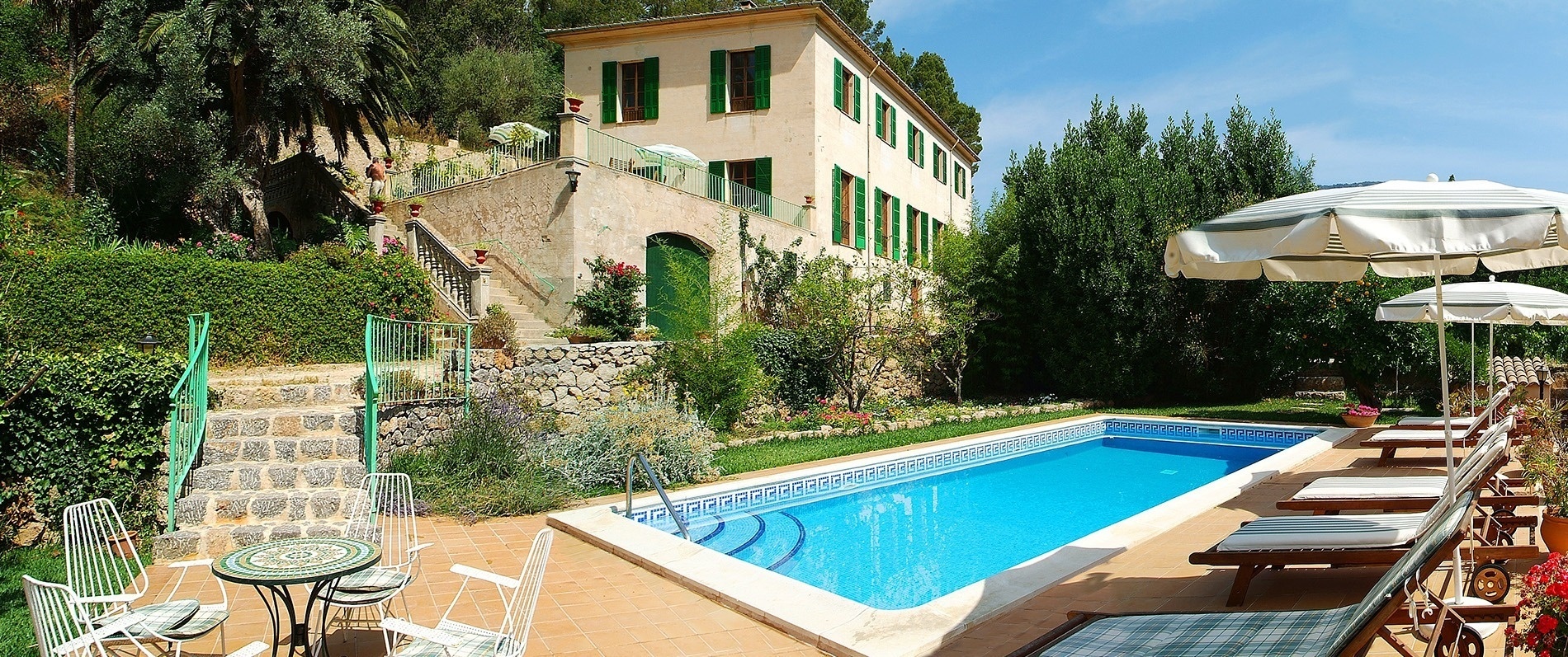 una piscina rodeada de muebles y sombrillas con una casa en el fondo