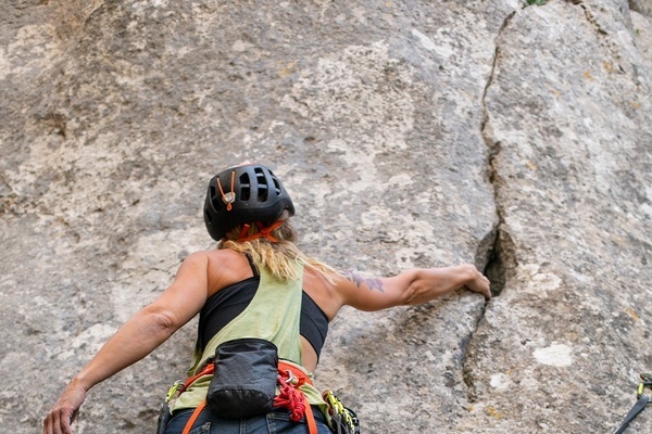 una mujer con un casco y una camiseta verde sube una pared de roca