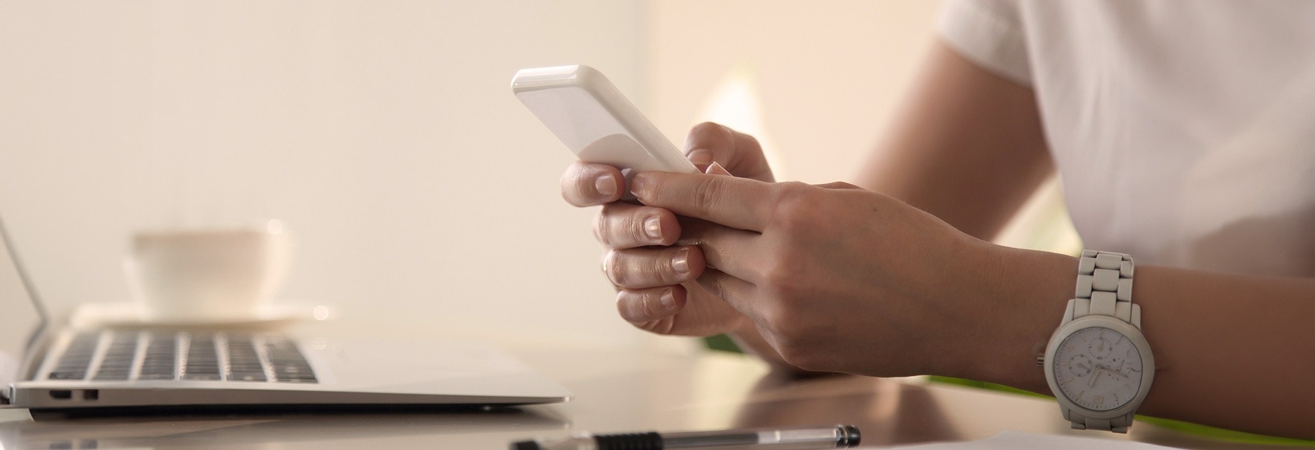 una mujer sostiene un teléfono celular frente a una computadora portátil