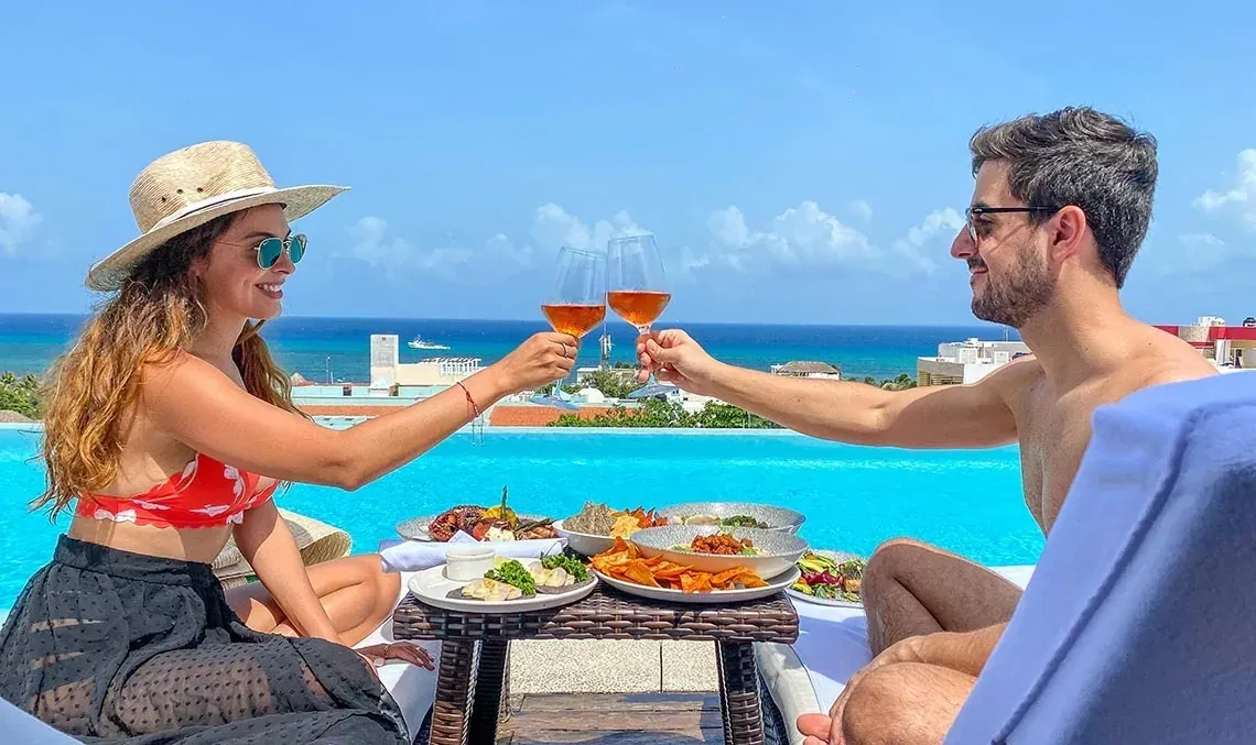Couple toasting with drinks at The Fives Downtown Hotel - Curio Collection by Hilton rooftop pool.