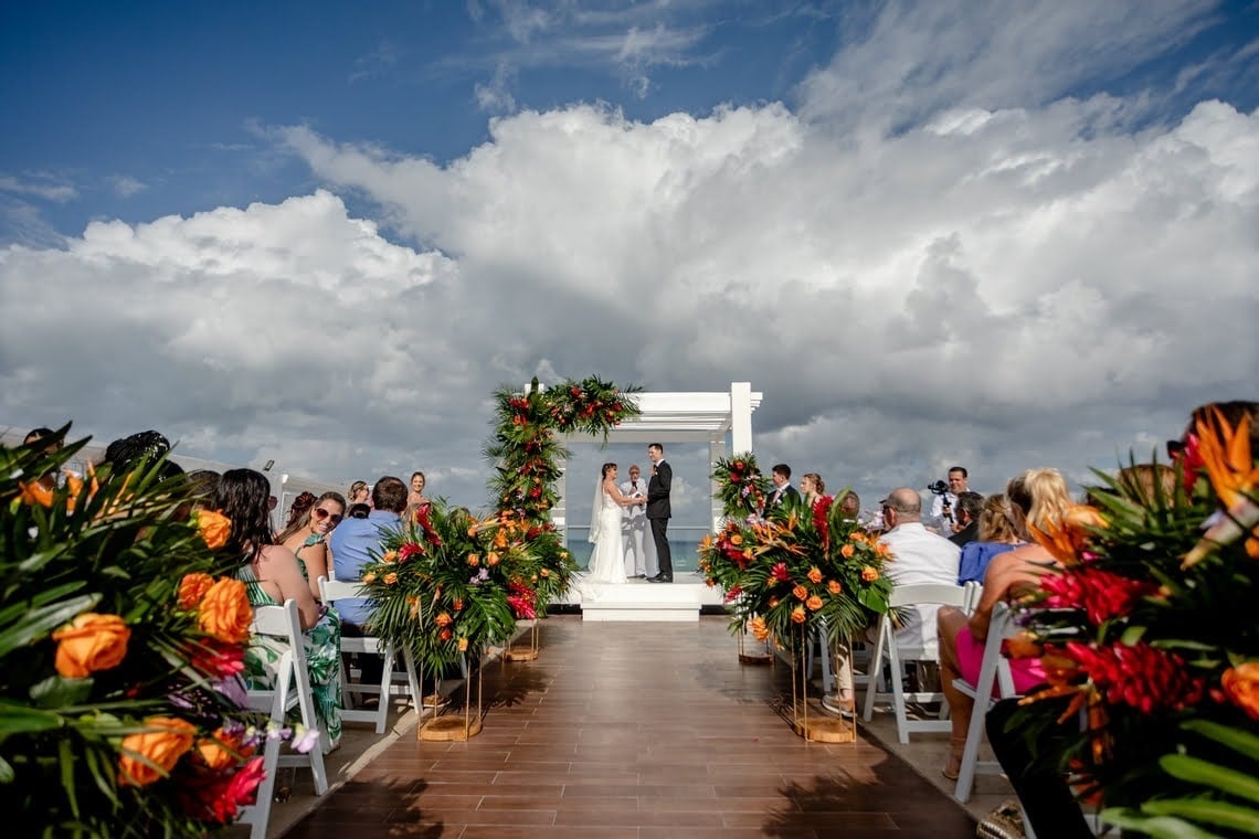 a bride and groom walking on the beach at sunset