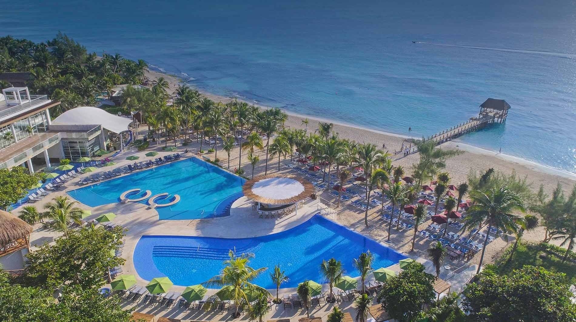 an aerial view of a beach resort with swimming pools and umbrellas