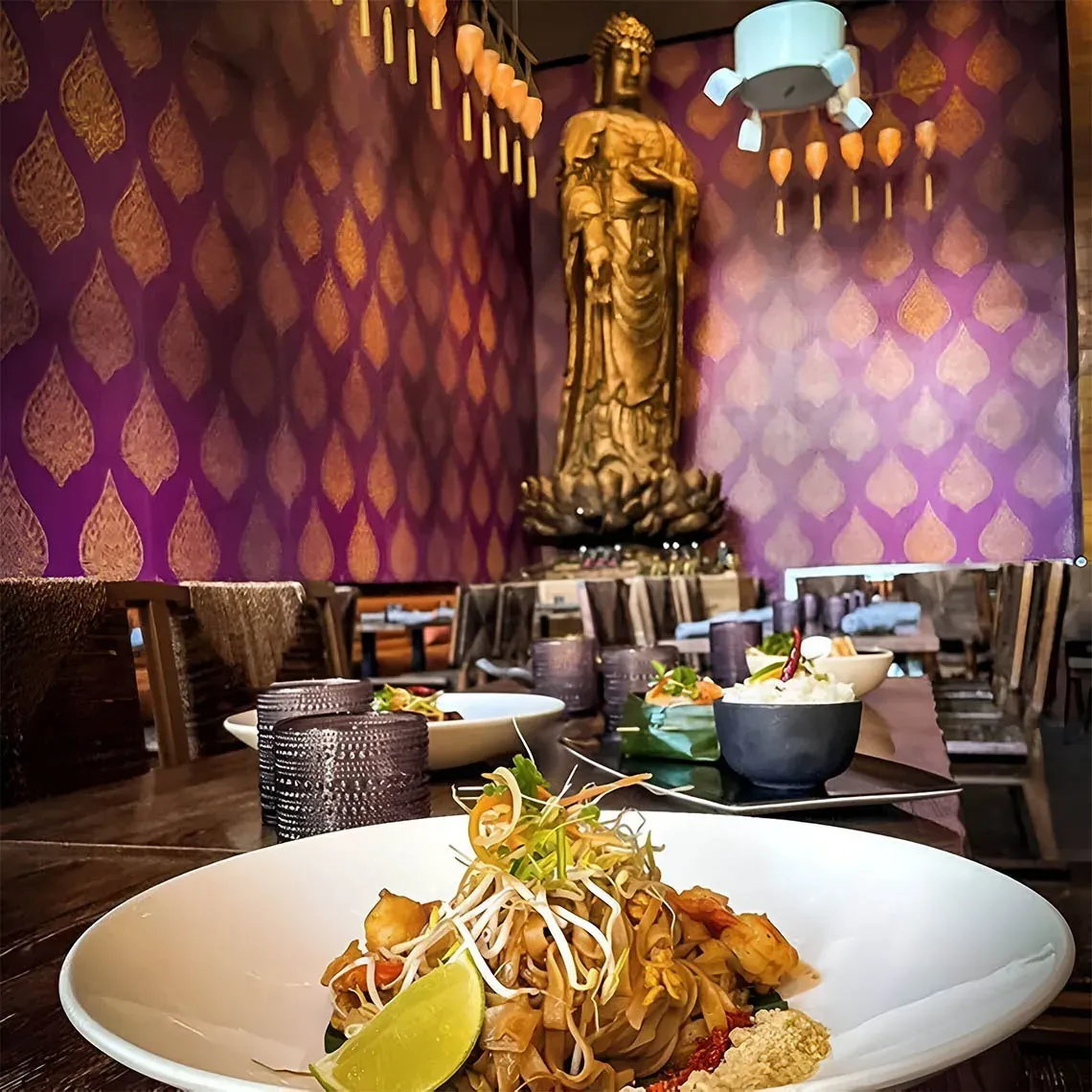 Elegant dining room at The Fives Corpo with golden Buddha and Pad Thai dish.
