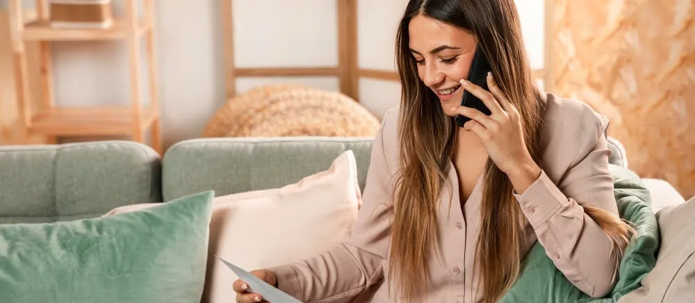 Contact us: Woman on phone with documents, relaxing on a sofa at The Fives Hotels Mexico.